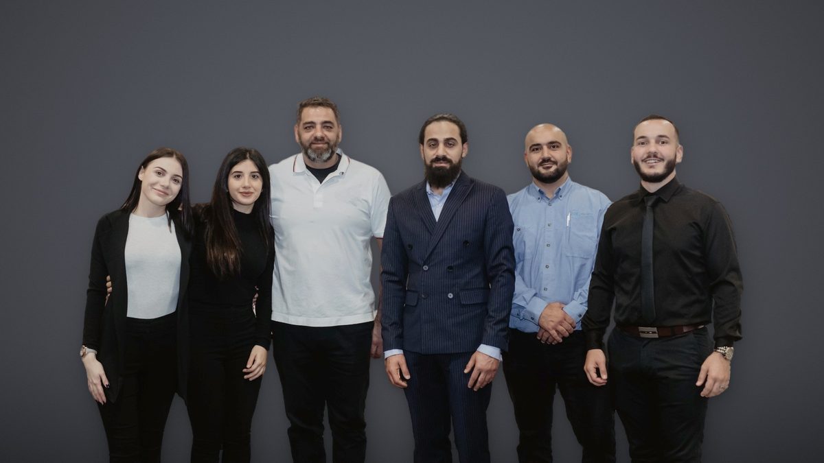 The KRAFTIGS management team, six people standing in a row against a graphite backdrop. In the centre, in a navy pinstripe suit, is Chief Executive Officer Ali Hammoud.